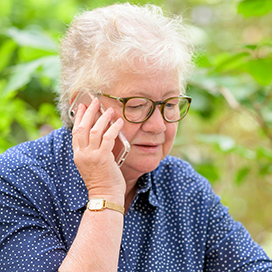 An elderly woman talking on the phone outside