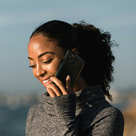 A woman smiling whilst holding a mobile phone up to her ear